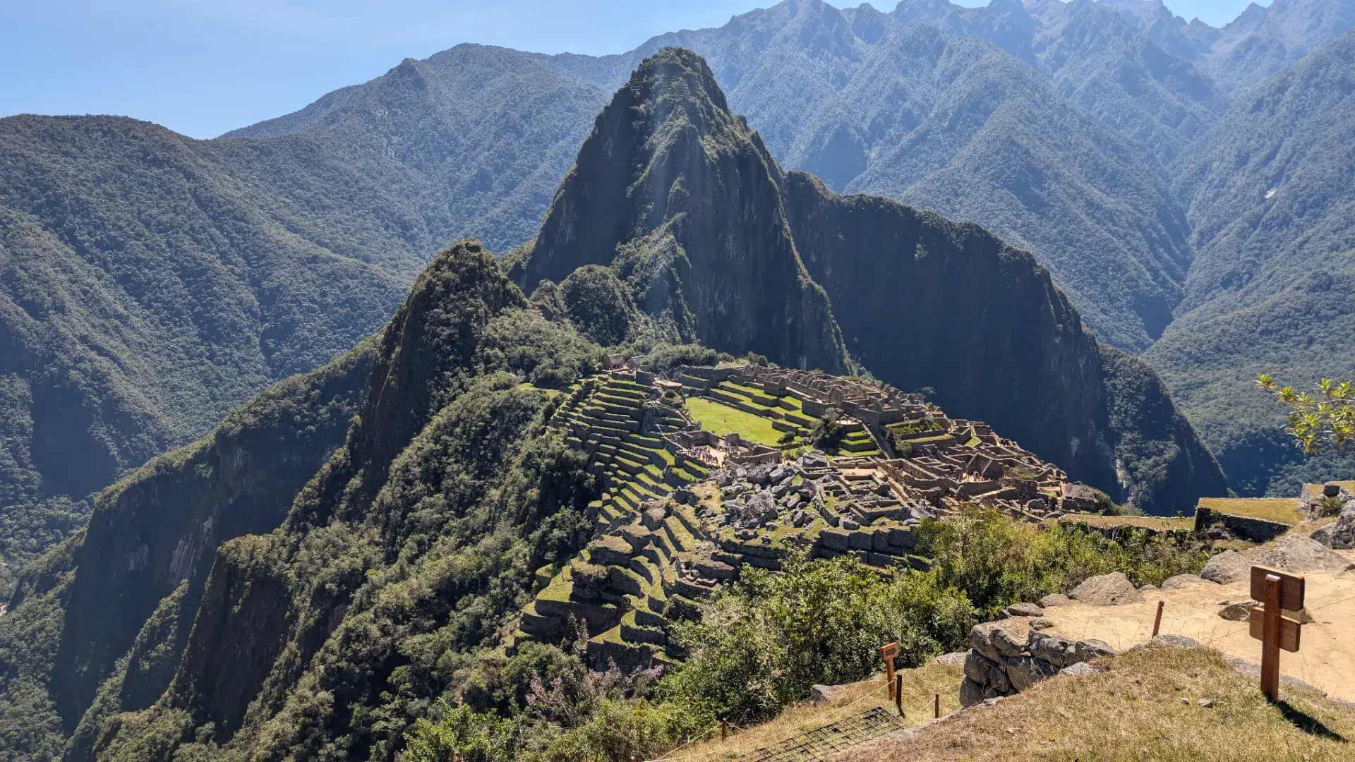 登山を終え、再び間近に仰ぎ見るマチュピチュ遺跡の全景。鋭く切り立ったワイナピチュ山を背景に、山の稜線に沿って整然と築かれた石造りの街並みが、午後の柔らかな陽光に照らされています。手前の段々畑から奥の神殿群まで、そのすべてが周囲の峻険な自然と見事に調和しており、インカの人々が抱いた自然への畏敬の念が伝わってくるようです。