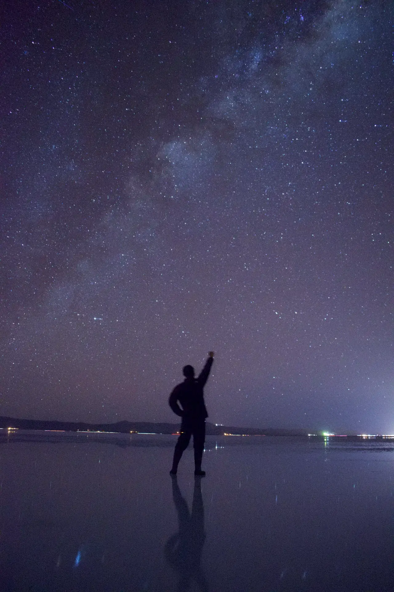 ウユニ塩湖の漆黒の夜、天の川が圧倒的な光の帯となって天空を貫いています。静止した薄い水面は、一等星から微細な星屑までを余すところなく映し出し、地平線の境界線は完全に消失。その無限の宇宙の真ん中に一人の旅人が立ち、拳を突き上げて自然の驚異を全身で受け止めています。166枚目のメニューで「スターライト」プランを選び、氷点下の寒さに耐えて待った者だけが出合える、この世のものとは思えない奇跡の光景。地球の鼓動と宇宙の広大さが一体となった、旅の最高到達点です。