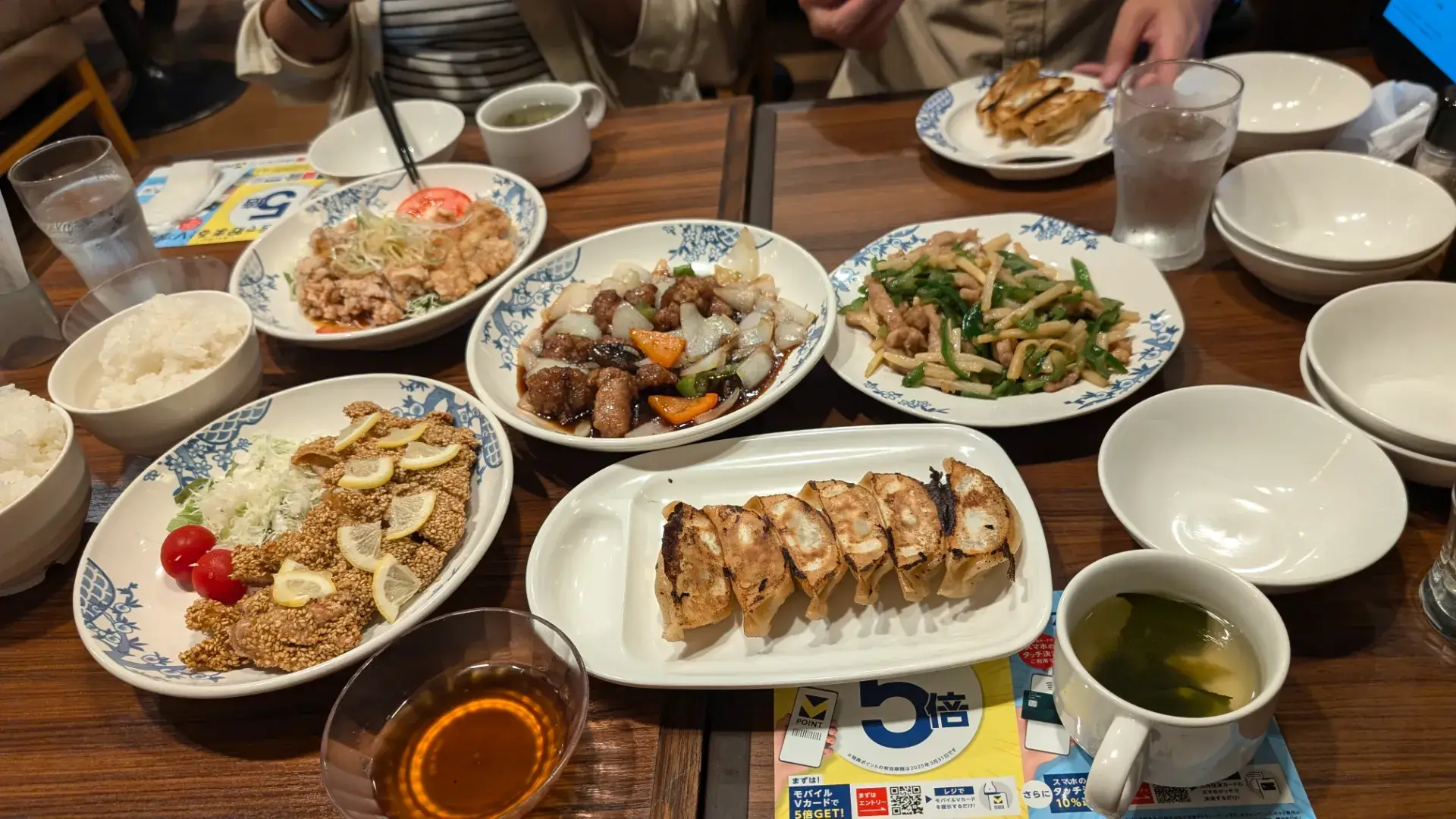 バーミヤン 富士急ハイランド駅前店の店内で、本格焼餃子、青椒肉絲、油淋鶏、黒酢の酢豚などの人気中華メニューがテーブルいっぱいに並んだ様子。家族や友人と囲む賑やかな夕食の風景。