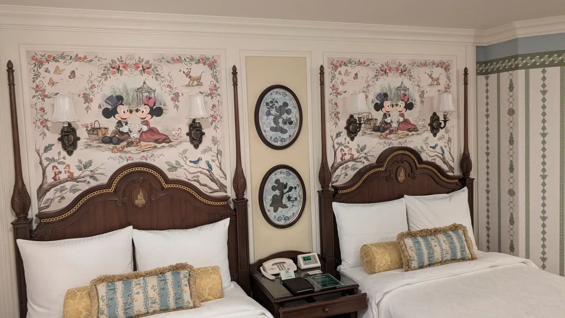 ツインベッドのヘッドボード上にある、ピクニックをするミッキーとミニーのクラシックな壁画。物語の中に泊まる体験を象徴する一枚。