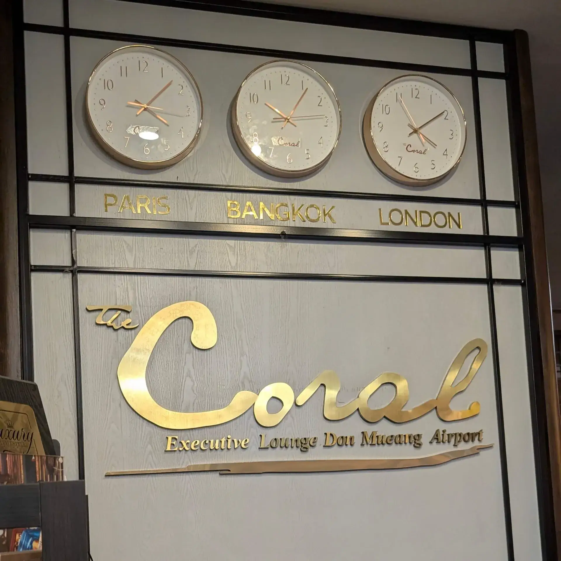 ドンムアン空港内にある「コーラル・エグゼクティブ・ラウンジ」のスタイリッシュな壁面。パリ、バンコク、ロンドンの時刻を刻む3つのゴールドの時計が並び、国際空港らしい旅情を誘います。下部にはラウンジのロゴが誇らしげに掲げられ、落ち着いた色調のデザインが、搭乗前のひとときを優雅に演出します。スコータイから始まった長く充実した旅の終わりを前に、静かに思い出を振り返るのにふさわしい上質な空間です。