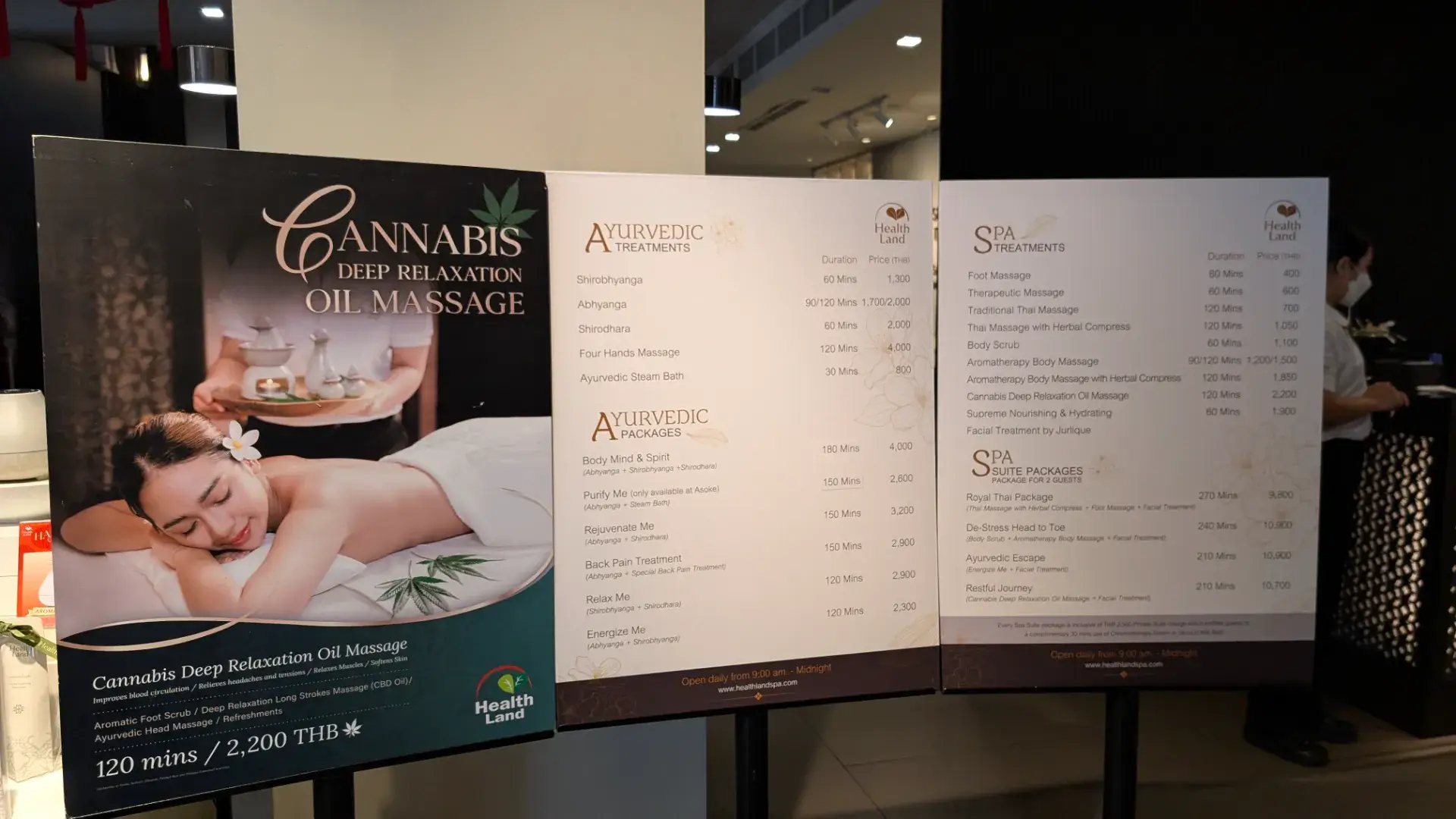 ヘルスランド・スパ・アソークの受付に設置されたメニュー表。伝統的な「タイ古式マッサージ（120分/700THB）」や「フットマッサージ」といった定番から、本格的な「アーユルヴェーダ」、さらには「大麻（Cannabis）ディープリラクゼーション・オイルマッサージ（120分/2,200THB）」といった最新のウェルネスメニューまで、豊富な選択肢が並びます。明朗会計で時間と料金が分かりやすく、旅の予算や疲れ具合に合わせて最適なケアを選べるのが魅力です。