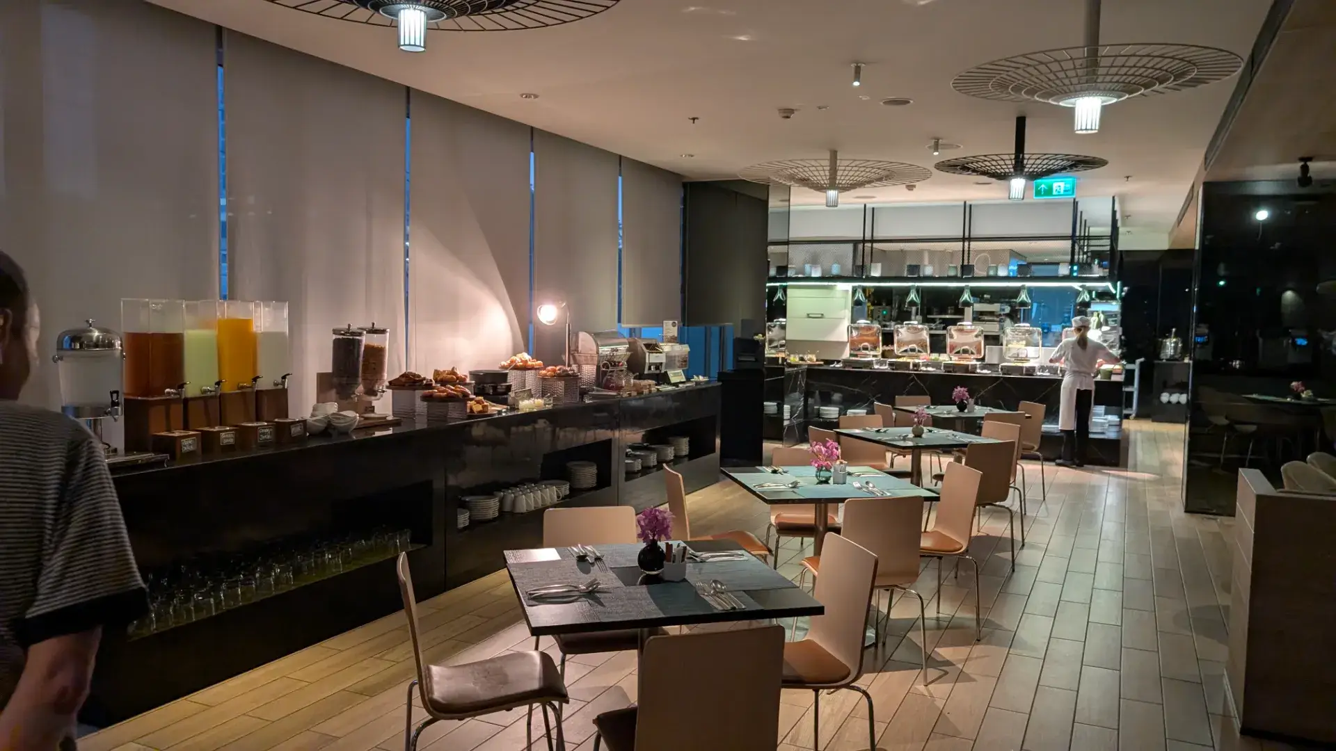 「モデナ バイ フレイザー バンコク」内のレストランで提供される朝食ビュッフェの様子。シックなインテリアの店内には、新鮮なフルーツジュースやシリアル、焼きたてのパンなどが美しくディスプレイされています。オープンキッチンスタイルで、都会的な雰囲気の中でゆったりと一日の活力を蓄えられる、宿泊者にとって楽しみなひとときです。