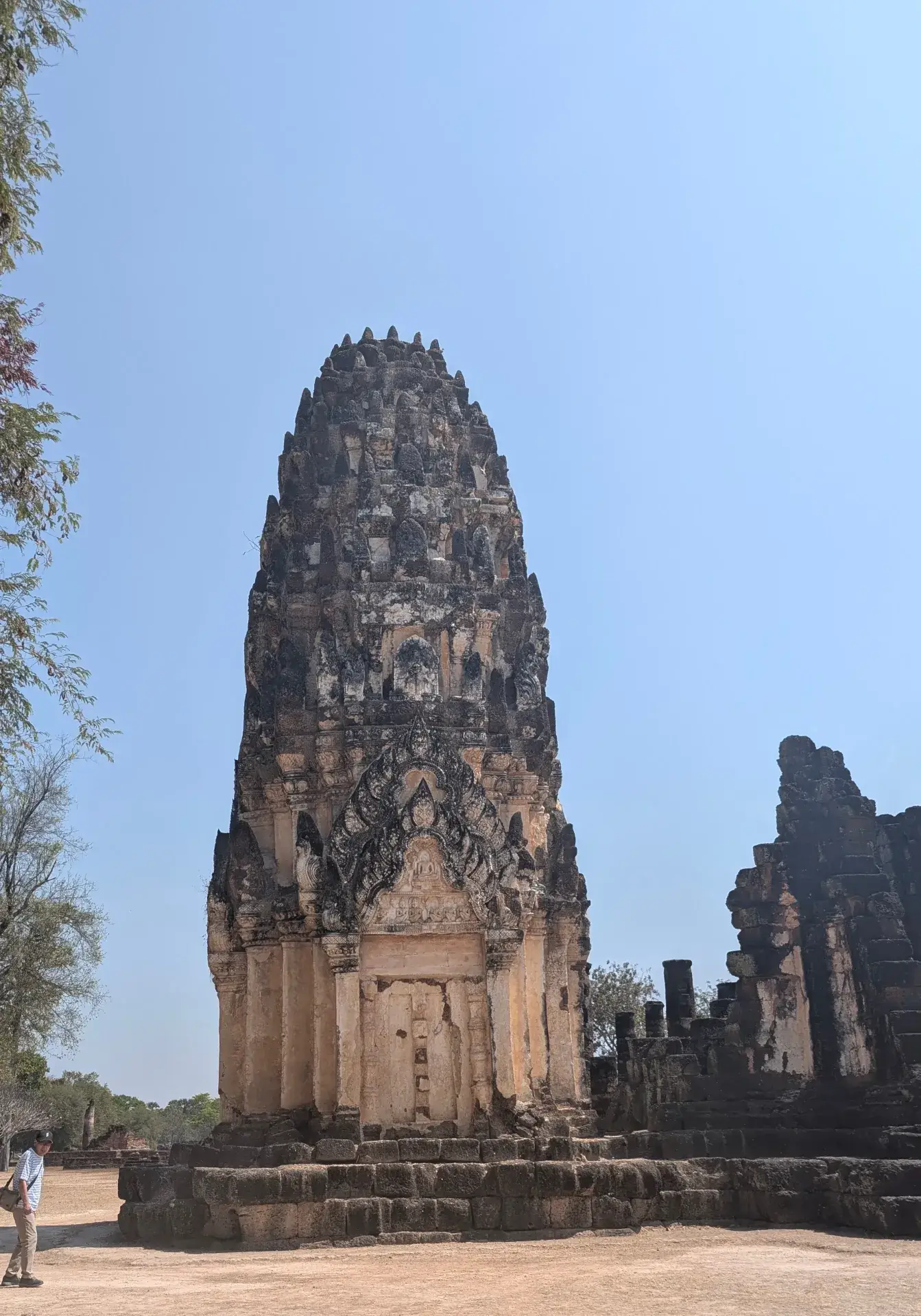 タイのスコータイ歴史公園内にある、クメール様式の影響を受けたトウモロコシ型の仏塔（プラーン）。緻密な彫刻が施された石造りの外壁が重厚な歴史を感じさせ、青く澄み渡った空とのコントラストが美しい、タイを代表する仏教建築の遺構です。