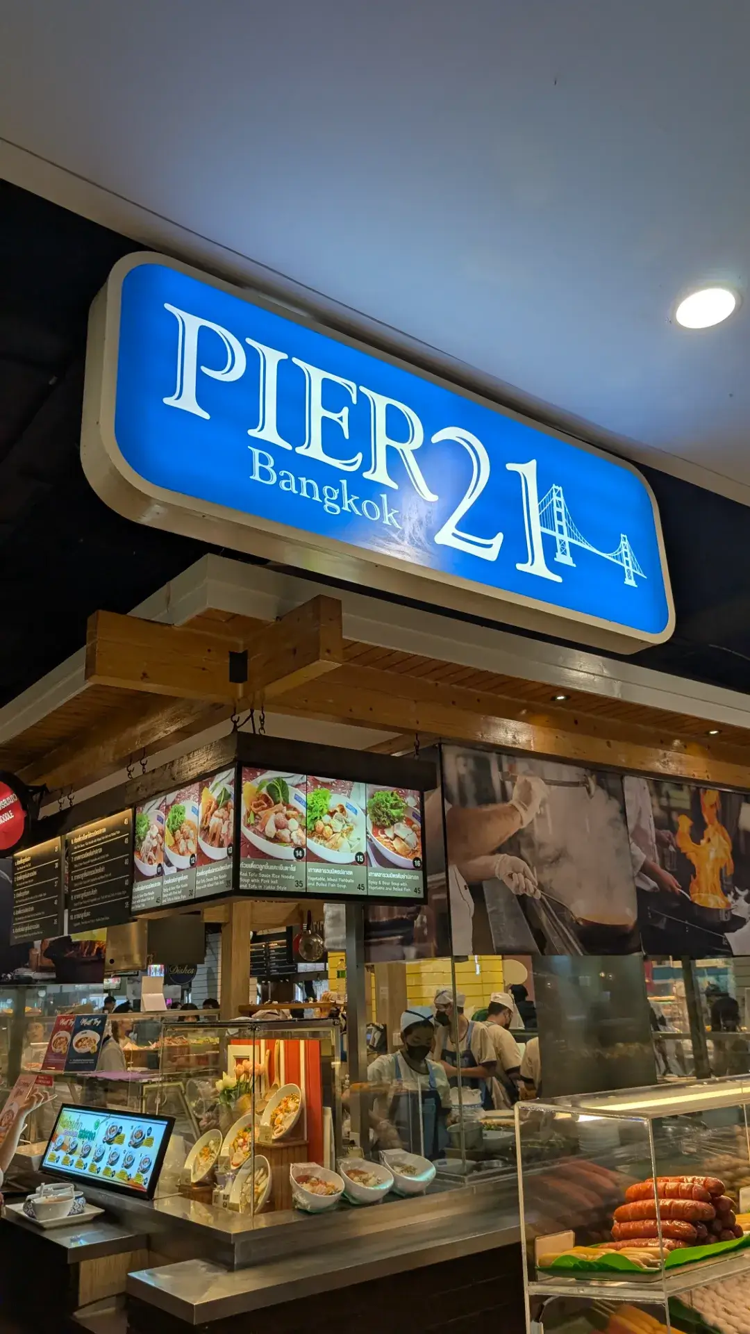 バンコクのアソーク駅直結のショッピングモール、ターミナル21の5階にある巨大フードコート「PIER 21（ピア21）」の鮮やかなブルーの看板。サンフランシスコのフィッシャーマンズワーフをイメージした内装で、活気に満ちています。バンコク屈指の低価格で本格的なタイ料理を楽しめることで有名で、地元の人から観光客まで、多くの人々が美味しい食事を求めて集まるグルメの聖地です。