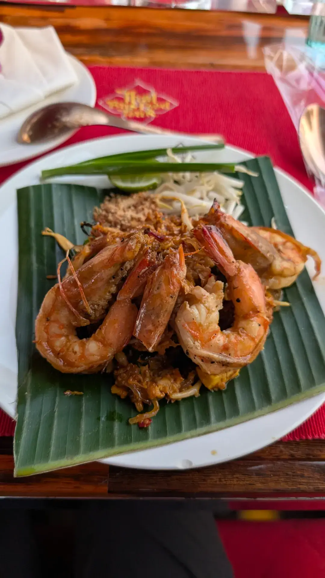 「タイ・バス・フードツアー」のメインディッシュとして提供された、ミシュラン・ビブグルマン掲載店「フェイ・タル（Fai Ta Lu）」のパッタイ。バナナの葉の上に美しく盛り付けられた麺の上には、大ぶりのエビが贅沢に並び、食欲をそそる香ばしい匂いが車内に広がります。伝統的な調理法にこだわった濃厚な味わいと、シャキシャキのモヤシやニラ、ライムの酸味の絶妙なハーモニー。バンコクの夜景を眺めながら味わうこの一皿は、食の都タイが誇る最高の美食体験です。