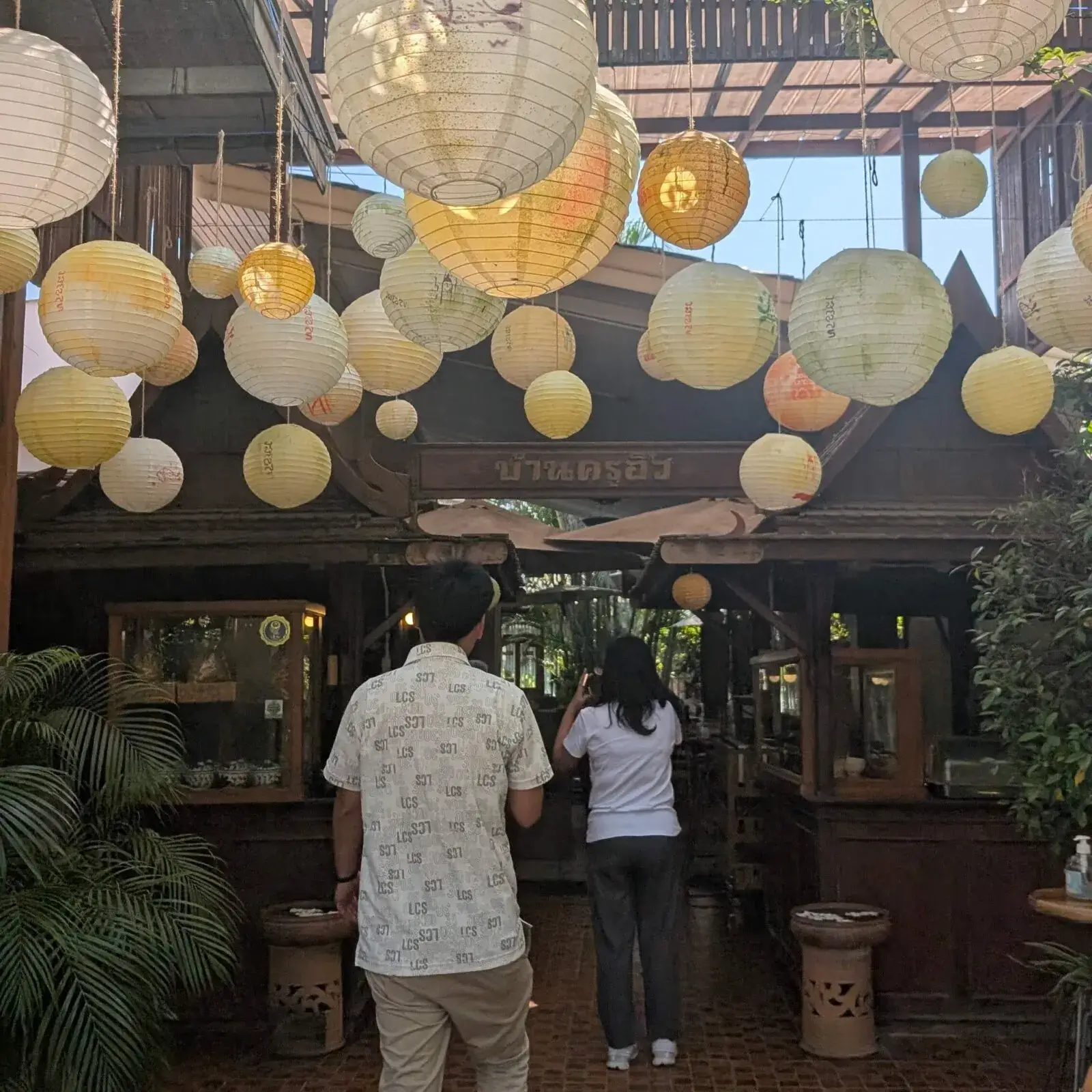 タイの伝統的な木造建築を活かしたレストランの入り口。頭上には大小さまざまな白い提灯が吊るされ、温かみのある光が空間を包み込んでいます。落ち着いた雰囲気の中で地元の料理を楽しめる、隠れ家のような情緒溢れるスポットを捉えた一枚です。