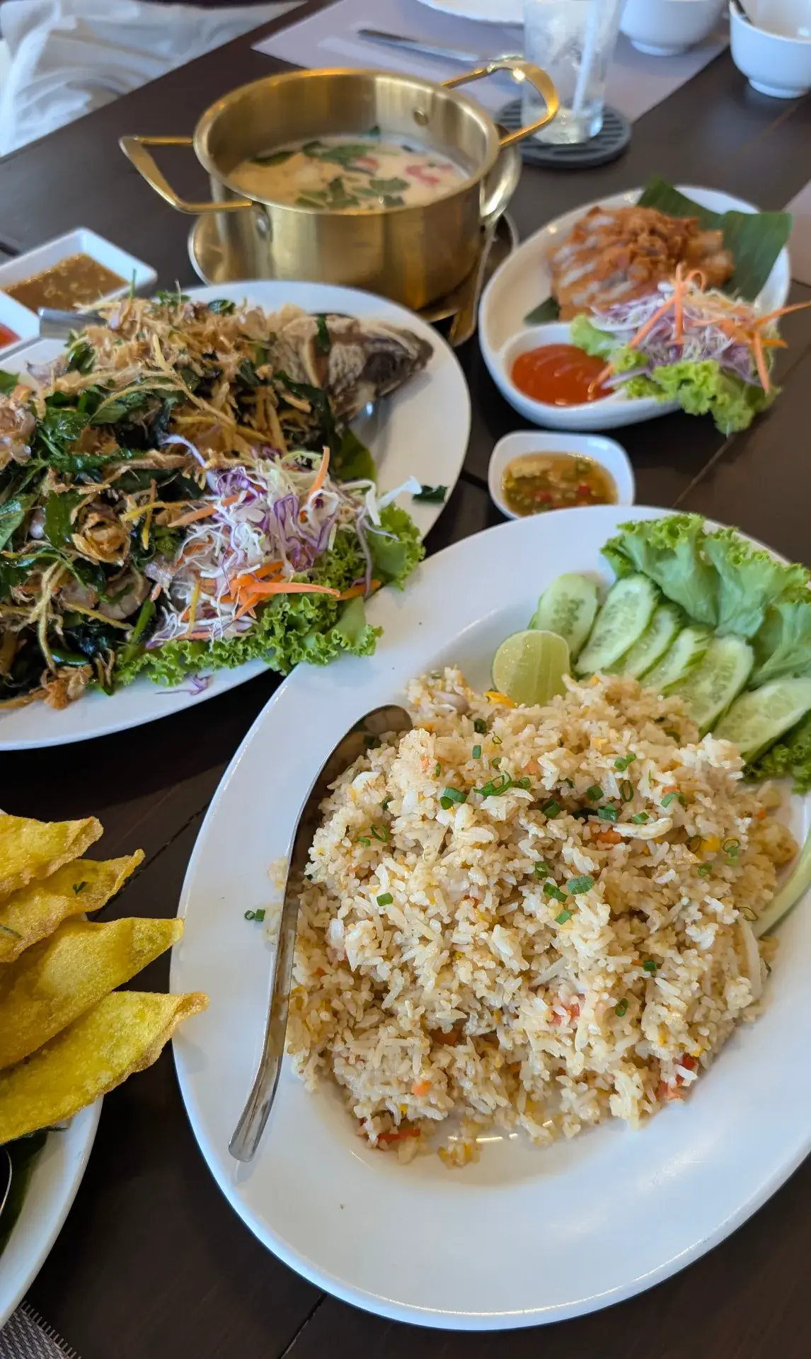 スコータイのレストランにて。山盛りのカオパット（タイ風炒飯）を中心に、背景には金色の鍋に入ったココナッツスープ（トムカーガイ）、ハーブたっぷりの魚料理、そしてサクサクの揚げ物が並ぶ、豪華な夕食のテーブル。