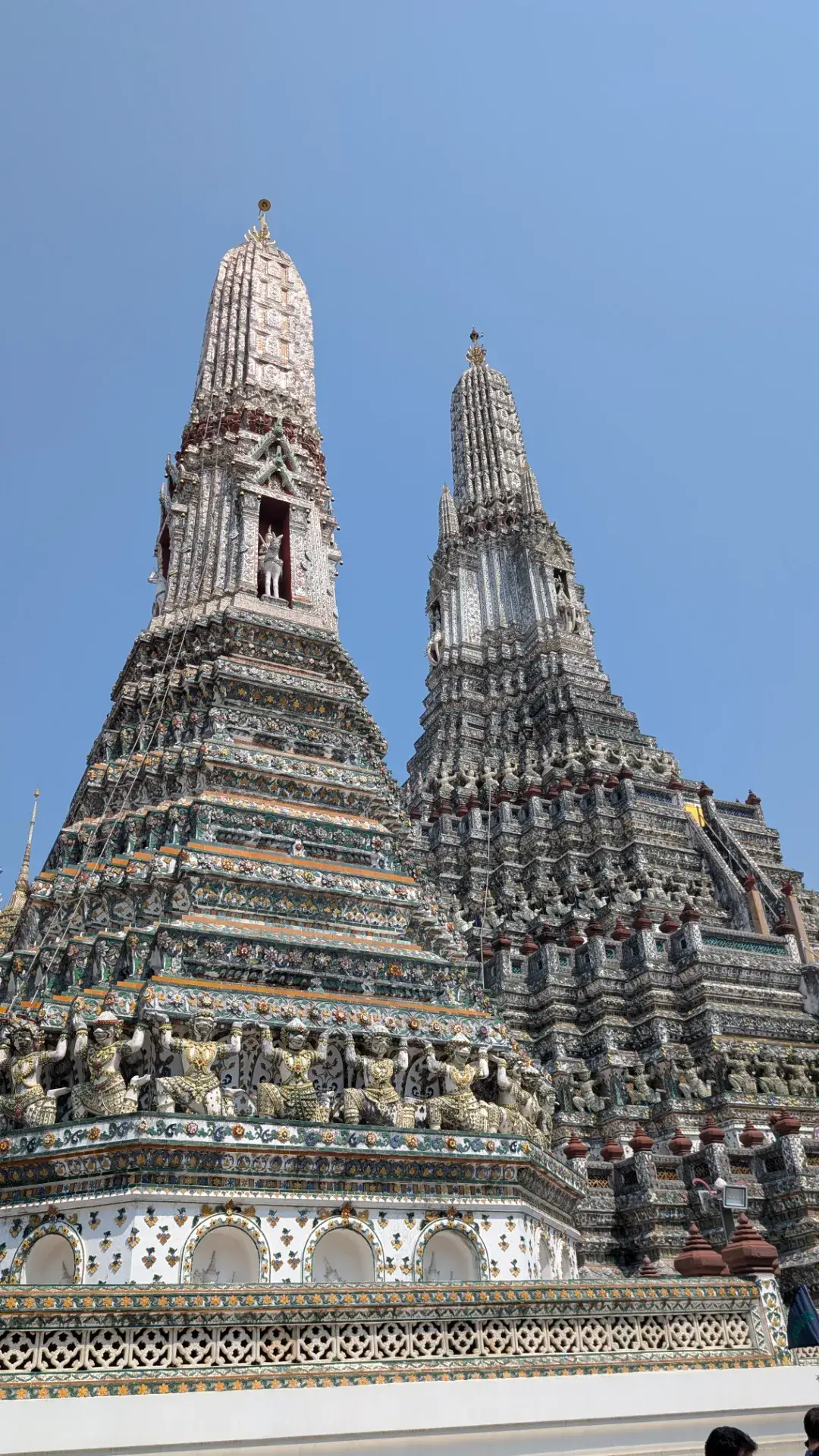 ワット・アルンの大仏塔の細部を捉えた一枚。仏塔の表面には、かつて中国からの船のバラスト（重り）として運ばれた陶磁器の破片が、色鮮やかな花模様のモザイクとして散りばめられています。下部では、仏塔を支えるように彫られた無数の神々や猿の像が並び、その圧倒的な密度と工芸技術の高さが、見る者を深く感動させる建築意匠です。