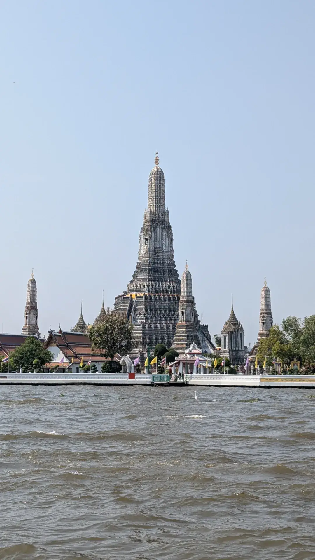 チャオプラヤー川のほとりに凛とそびえ立つ「ワット・アルン」。大仏塔を囲む4つの小仏塔が美しい対称美を描き、色とりどりの陶器片で装飾された表面が陽光に映えています。川の波立ちとともに捉えられたその姿は、三島由紀夫の小説『暁の寺』の舞台としても知られ、バンコクの悠久の歴史と優雅さを象徴する絶景