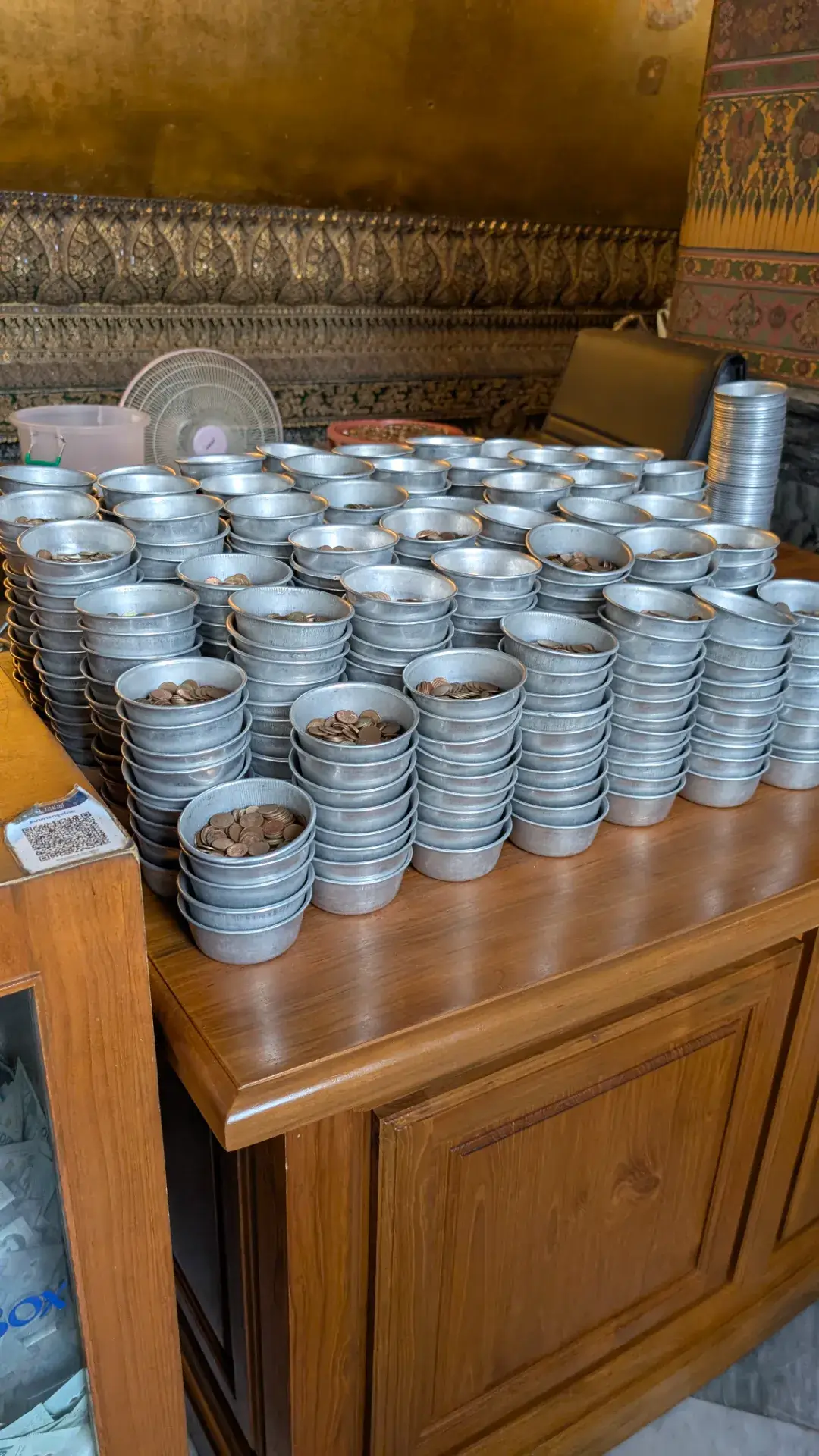 ワット・ポーの寝釈迦仏の背後の廊下にずらりと並んだ108つの青銅の鉢。参拝者は20バーツを小さなコインが入ったお椀と交換し、煩悩を捨て、徳を積む（タンブン）ために一つ一つの鉢にコインを投げ入れて歩きます。コインが鉢に当たる金属音が堂内に響き渡る、タイの伝統的な参拝の作法を捉えた一枚です。