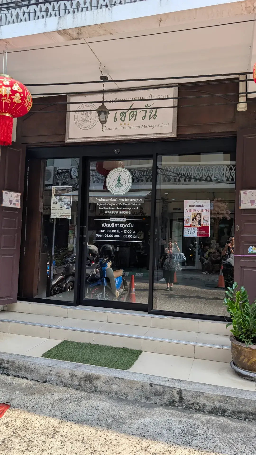 タイ古式マッサージの伝統を今に伝える「ワット・ポー・マッサージスクール（Chetawan Traditional Massage School）」の入り口。歴史を感じさせる木製の看板と、清潔感のあるガラス張りのエントランスが特徴です。朝8時から夕方まで営業しており、世界中から訪れる参拝客が、タイ最高峰の技術による本格的なマッサージで旅の疲れを癒やすために集まる、まさに「癒やしの聖地」の構えです。