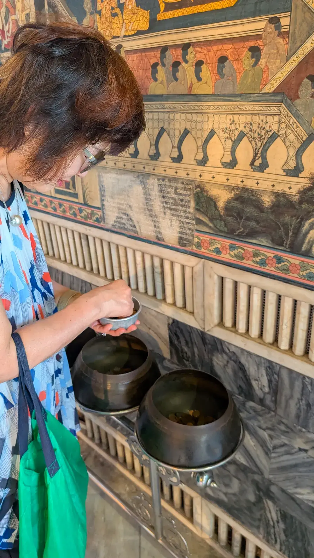 ワット・ポーの寝釈迦仏の背後に並ぶ108つの鉢に、一つずつ丁寧にコインを入れていく参拝の様子。この行為は、108の煩悩を一つずつ捨て去り、善行を積む「タンブン」というタイの仏教習慣に基づいています。美しい仏教壁画が描かれた廊下で、コインが鉢に響く音を聞きながら、自分自身と向き合う静かな時間を過ごしています。