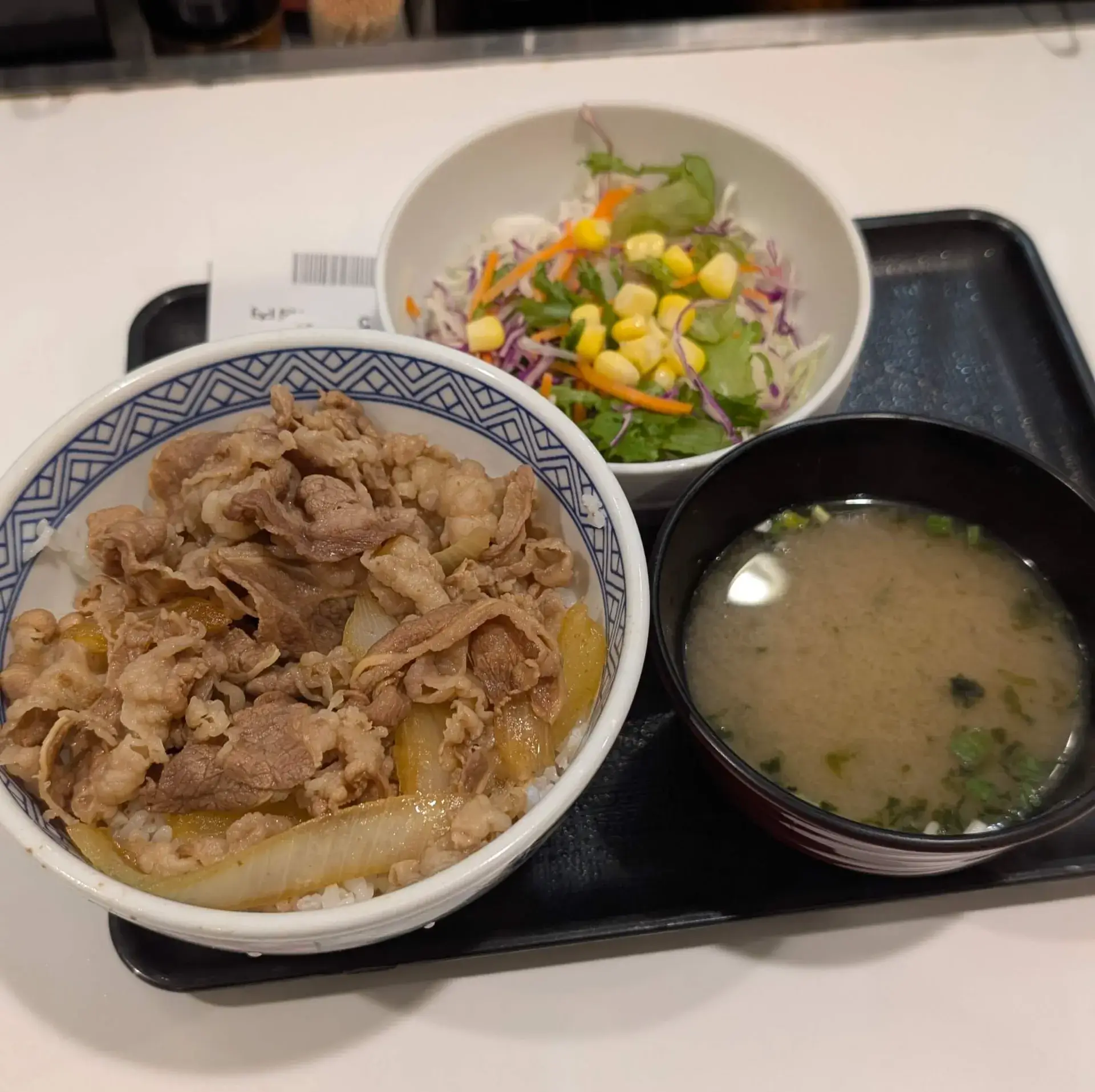 日本を代表するファストフード「吉野家」の牛丼セット。秘伝のタレで煮込まれた牛肉と玉ねぎがのった牛丼に、生野菜サラダと味噌汁が付いた、手軽で栄養バランスの良い定番の和食メニューです。
