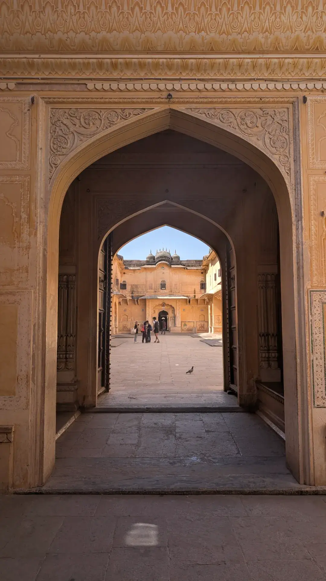 アンベール城の入り口にあるアーチ門から見た中庭の風景。石造りの門がフレームとなり、その奥に広がる広場と、歴史的な宮殿建築を正面から捉えている。