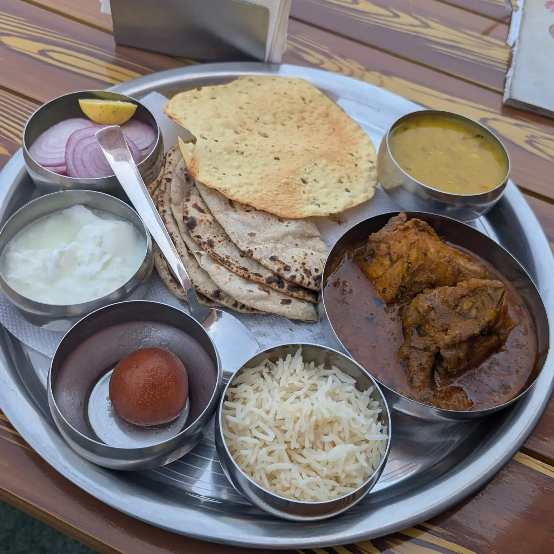 銀色のプレートに盛り付けられたインドのターリー定食。カレー、ライス、ロティ、パパド、デザートのグラブ・ジャムン。