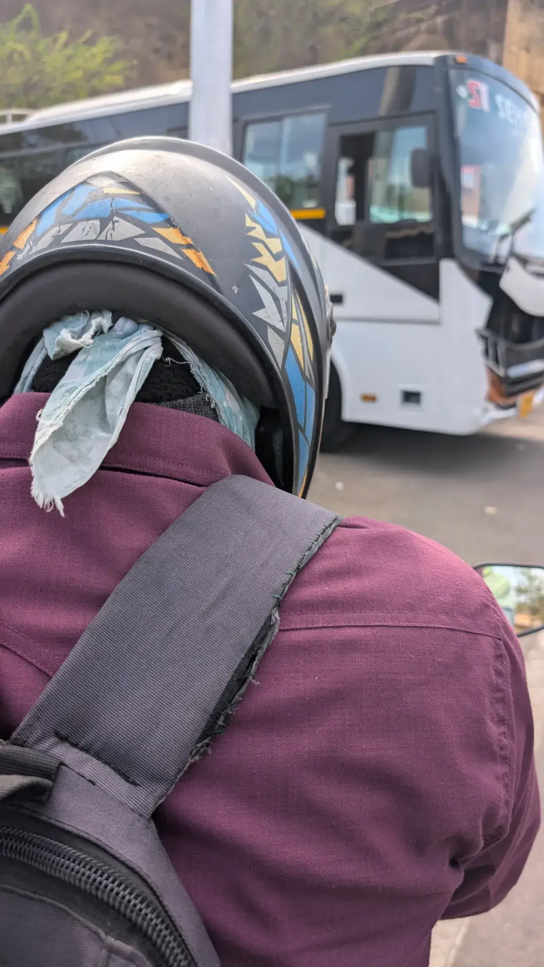 インドのデリーにて、Uber Moto（バイクタクシー）の後部座席から撮影された風景。ヘルメットを被りバックパックを背負った運転手の背中越しに、前方を走る白い大型バスが見える、活気ある道路の様子。