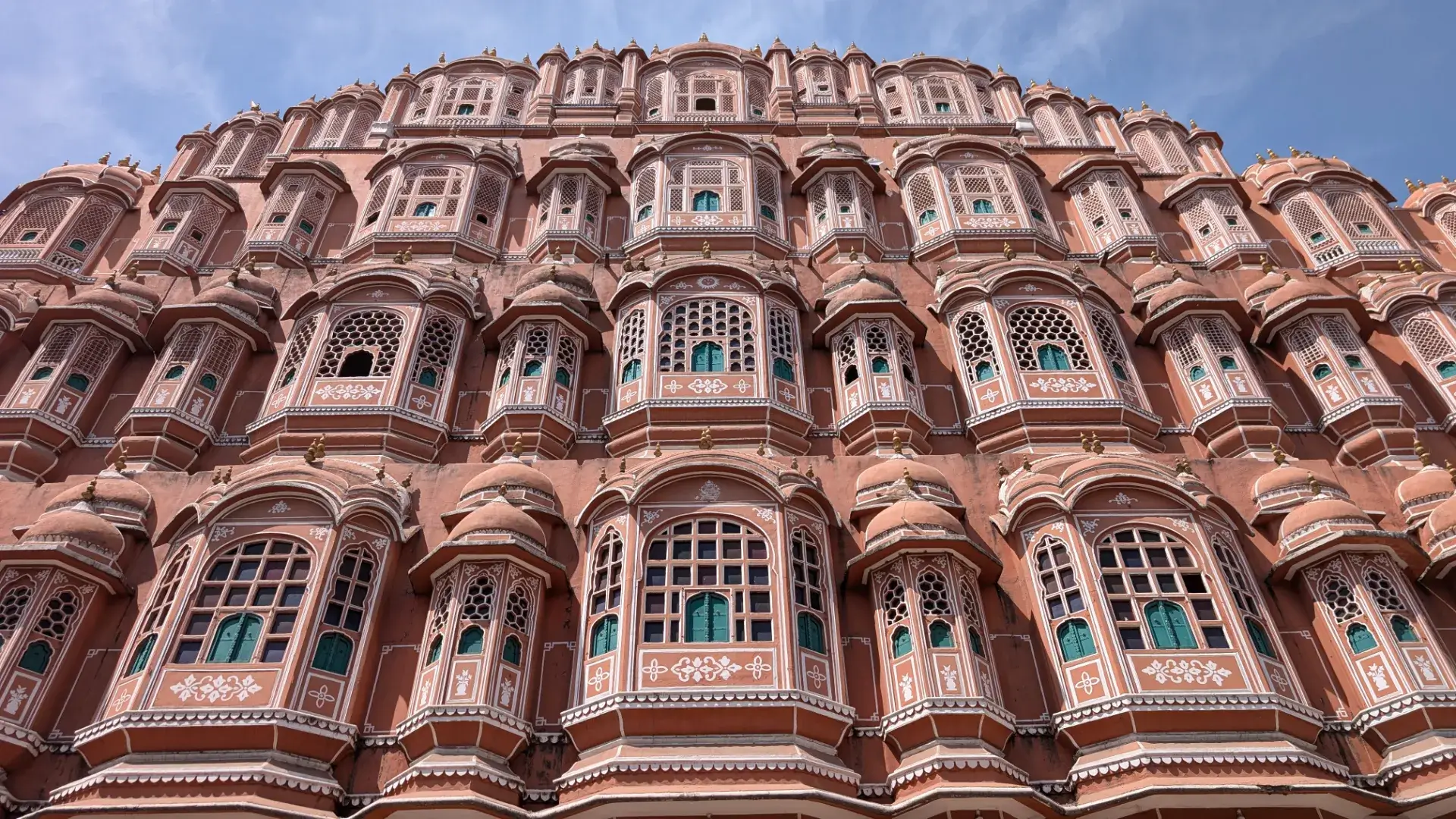 ジャイプールのウィンドビューカフェから間近に捉えたハワ・マハル（風の宮殿）。ピンク色の砂岩に施された無数の白い縁取り、繊細な格子窓（ジャロカ）、そして重なり合うドーム状の屋根が空に向かってそびえ立つ、圧巻の建築細部。