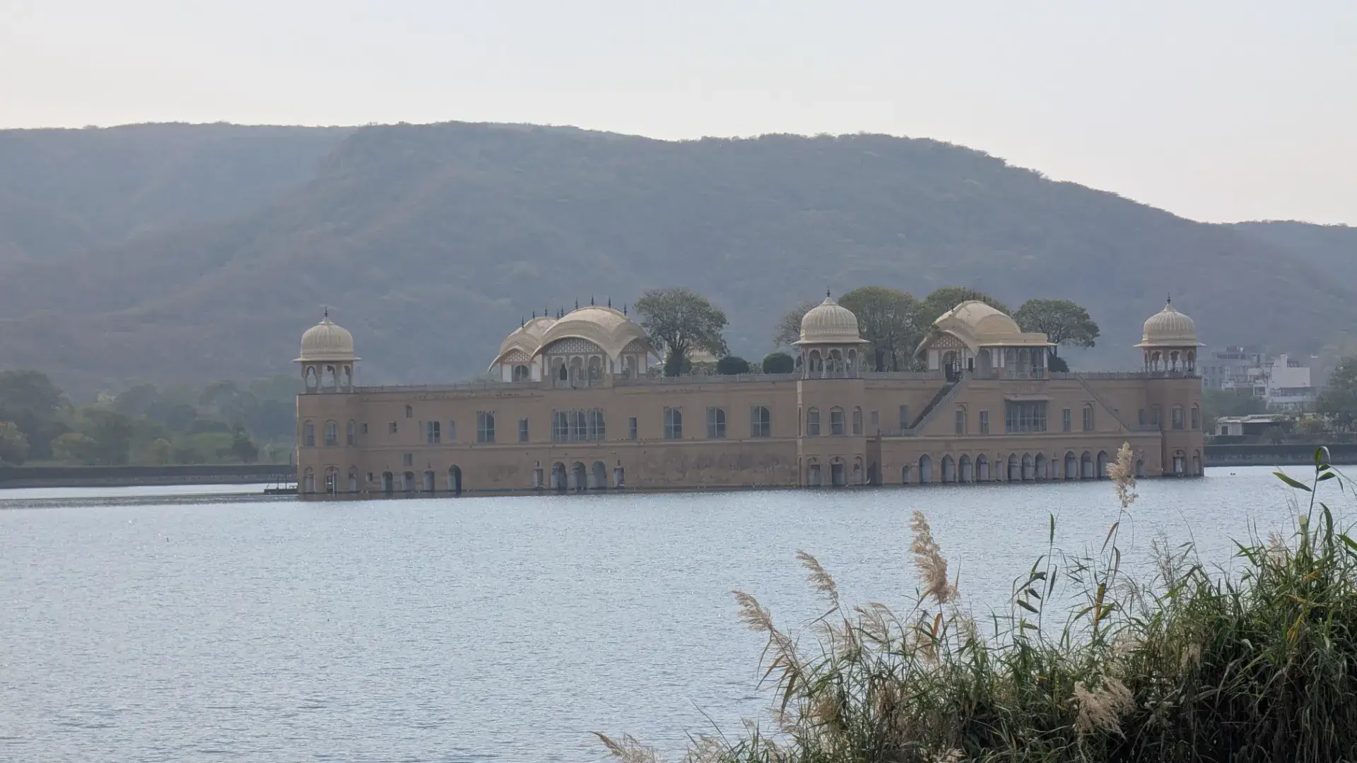 インド、ジャイプールのマン・サガール湖に浮かぶ「ジャル・マハル（水の宮殿）」のクローズアップ。砂岩で造られた4つのドーム状の屋根（チャトリ）と、水面に映る繊細なアーチ型の窓が特徴的なラージプート様式の建築美。