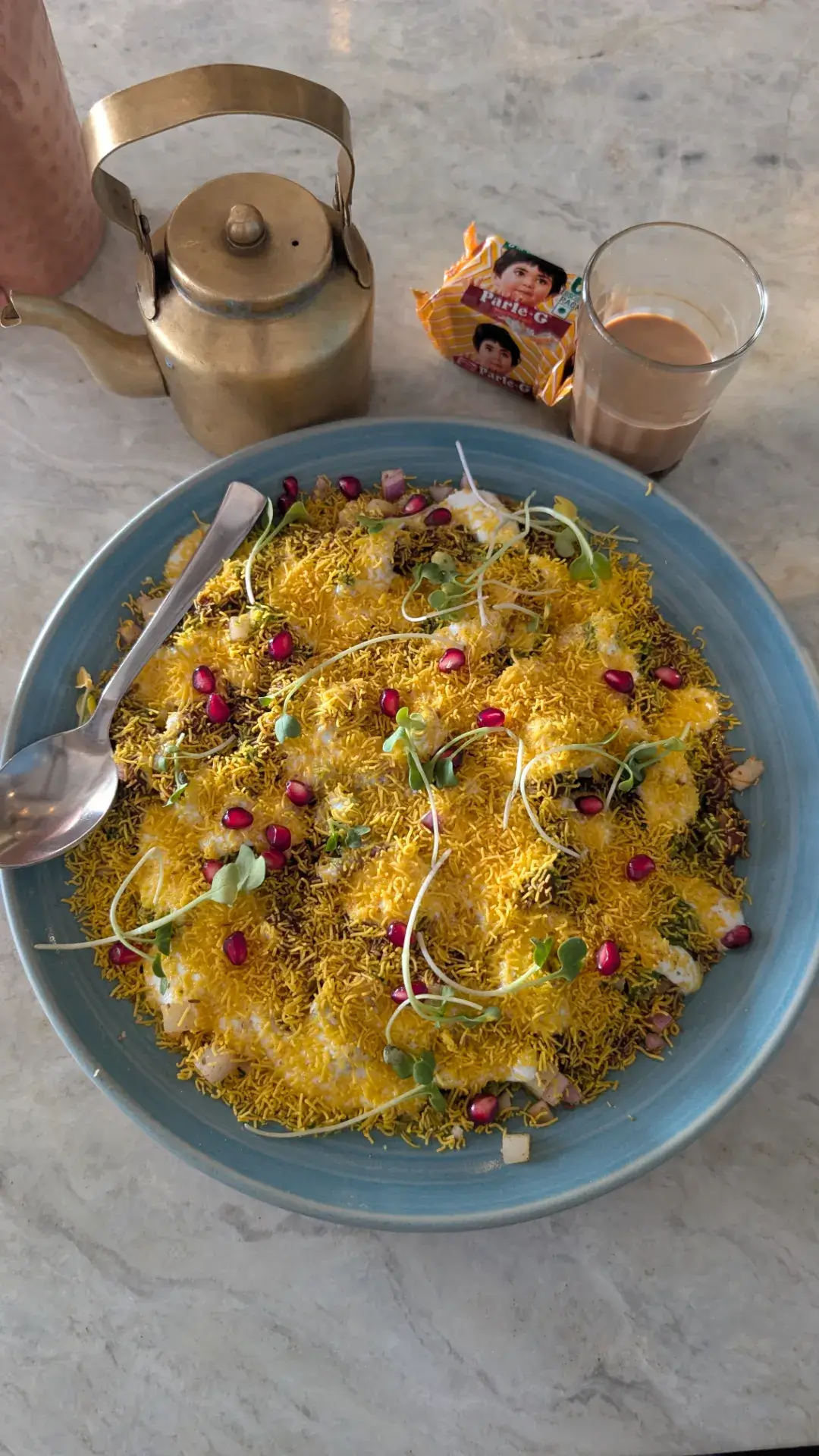 ジャイプールのカフェ「Tapri Central」で提供されたパプリ・チャート。青い大皿に盛られ、サクサクのパプリ（揚げせんべい）の上に、たっぷりのセブ（細い揚げ麺）、ヨーグルト、スパイス、そして宝石のようなザクロの粒とスプラウトが散りばめられた鮮やかな一皿。