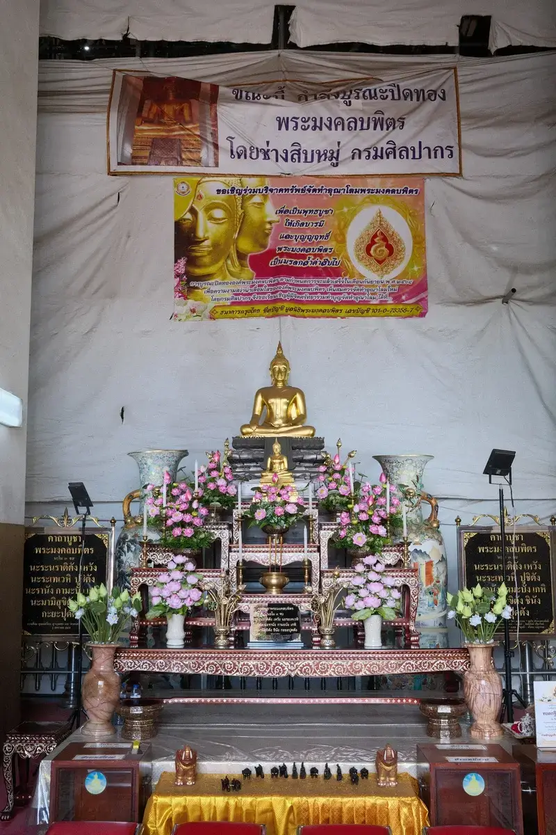 ワット・プラ・モンコン・ボピット(Wat Phra Mongkhon Bophit)の内部にある、金色の仏像と装飾された祭壇です。アユタヤ、寺院、内装といった文脈を含めています。