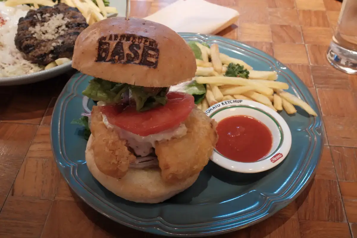 店名の刻印が入ったバンズのフィッシュバーガー。トマトとレタスがサンドされ、ポテトとケチャップが添えられたセット。