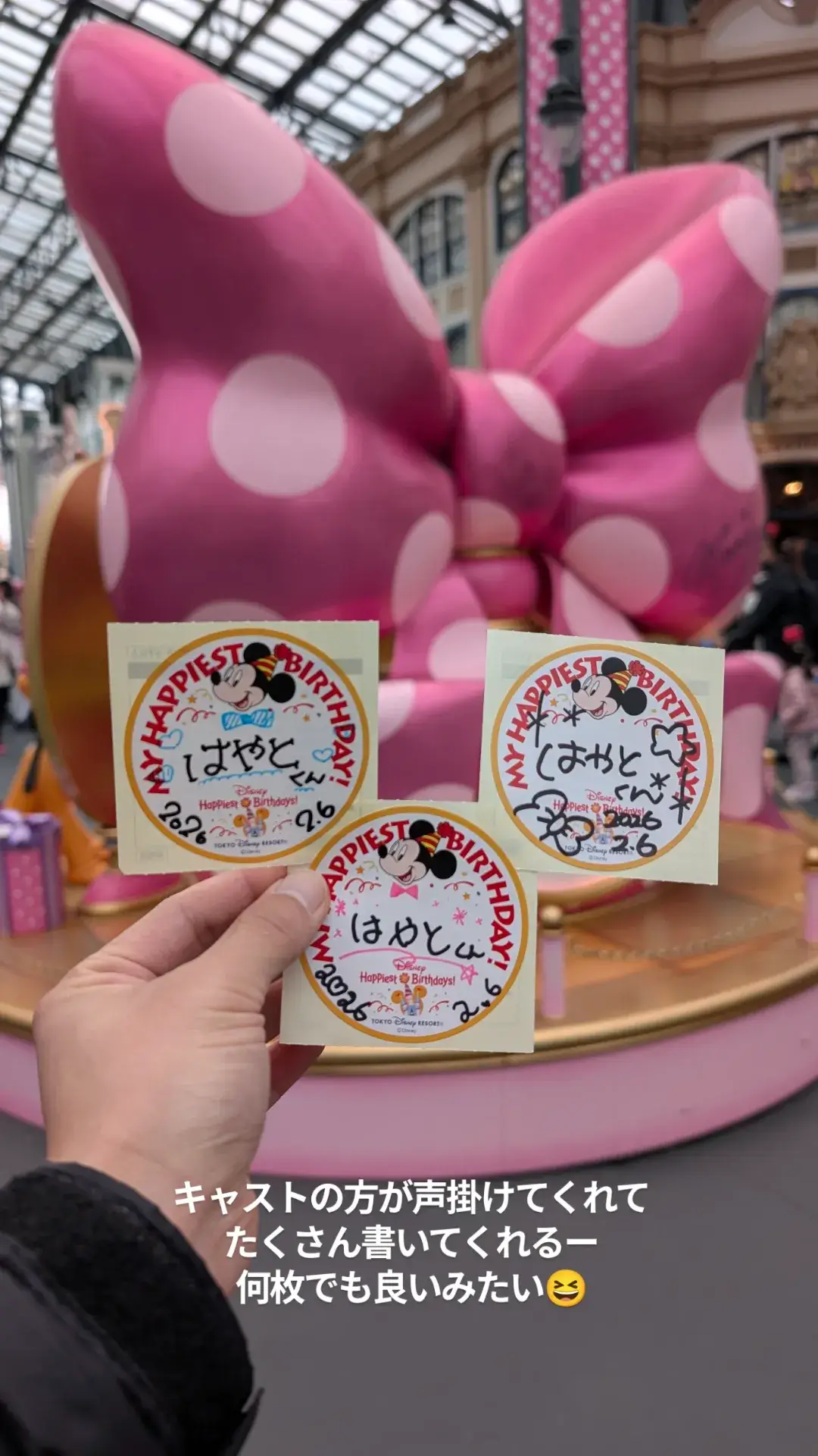 東京ディズニーランドでキャストに書いてもらった3枚のバースデーシールと背景に広がるピンクのミニーマウスのリボン型モニュメント